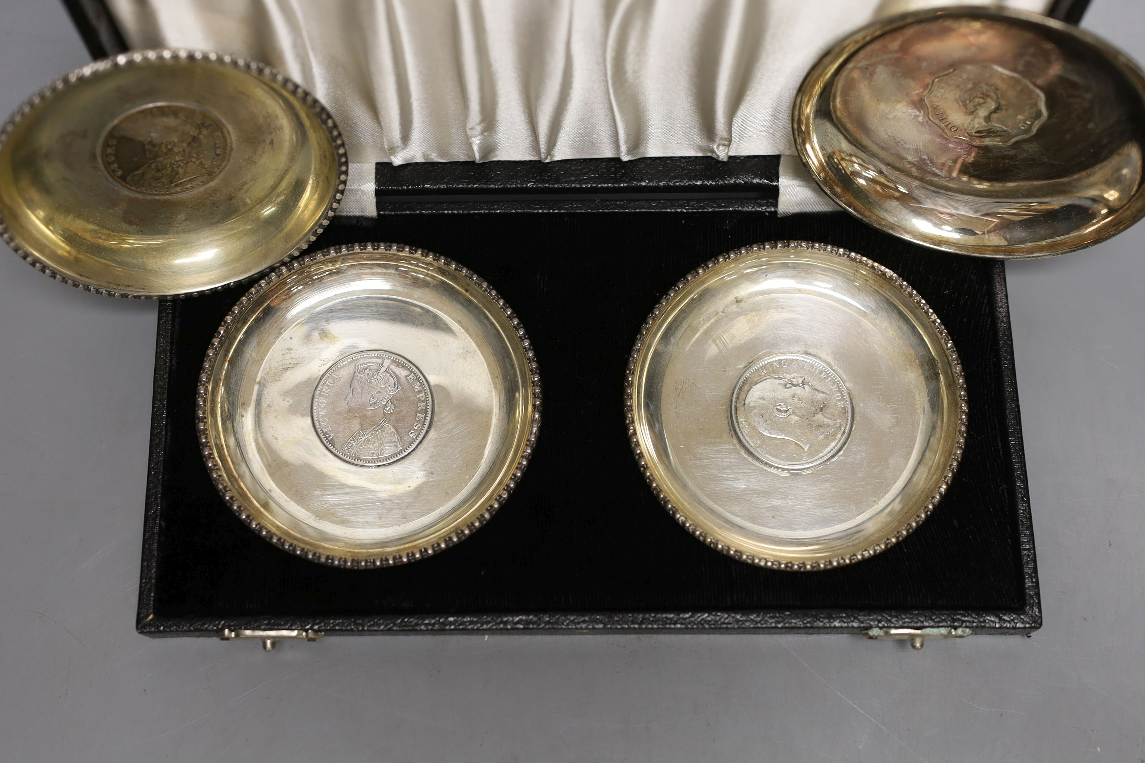 A cased pair of white metal inset coin small dishes and three other similar dishes.